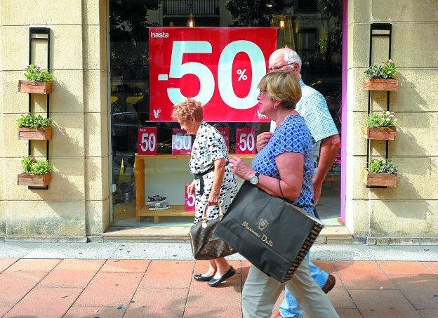 Ciudadanos pasean frente a un comercio que anuncia descuentos de hasta el 50%. 