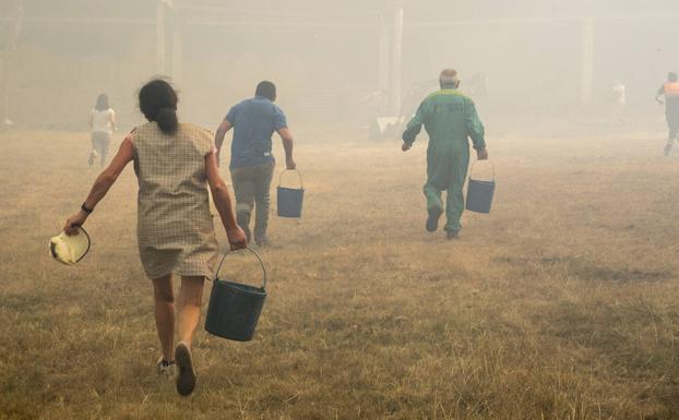 Vecinos del municipio lucense de Palas de Rei transportan cubos de agua para refrescar la zona de un incendio vecino.