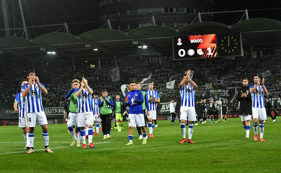 Los jugadores aplauden a la afición a la conclusión del partido, con el marcador que refleja el triunfo, detrás.