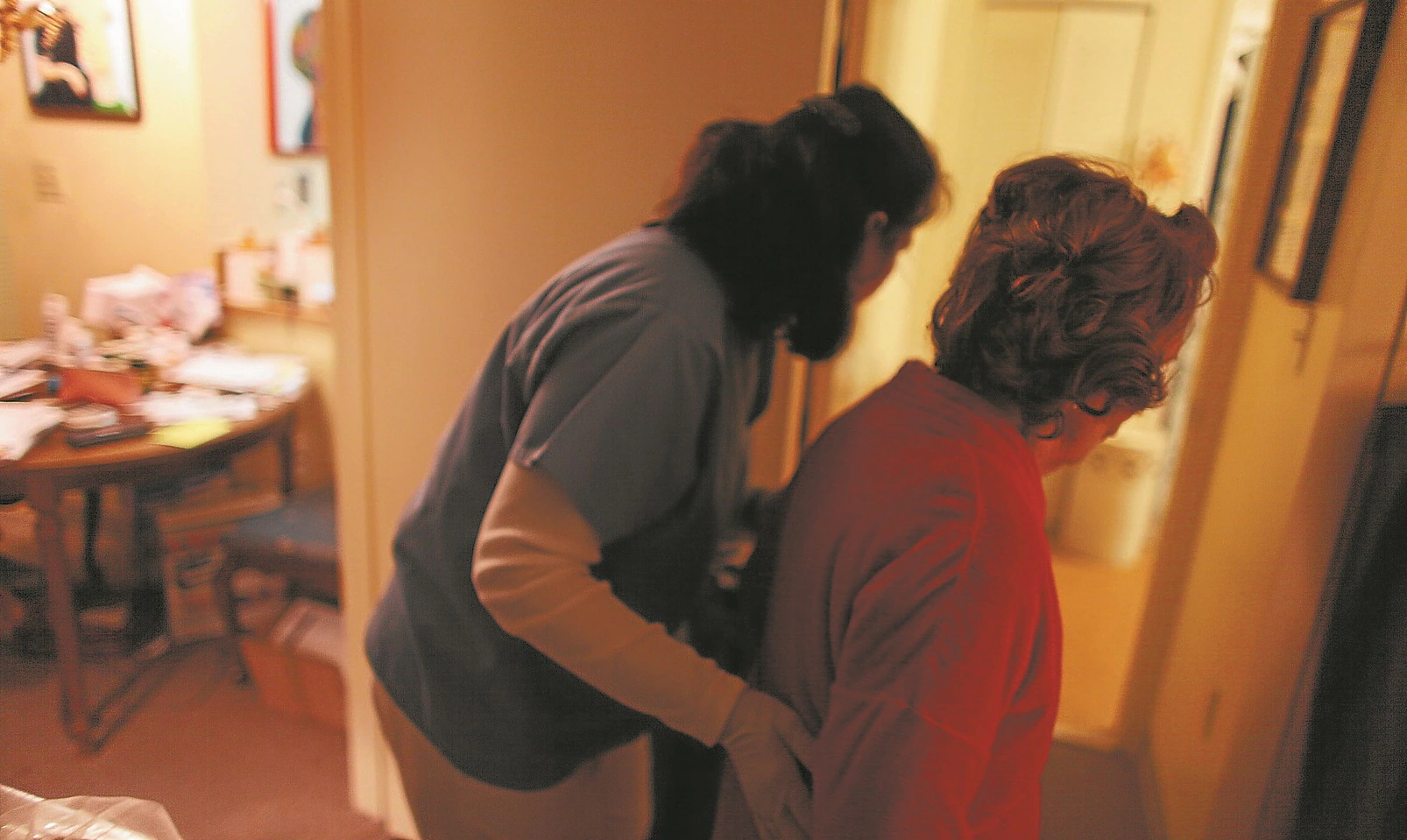 Una auxiliar acompaña a una mujer mayor al baño de su casa. /REUTERS