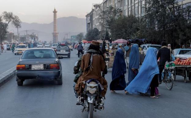 A group of women dressed in burqas cross a road in Kabul before two Taliban on motorcycles and armed. 