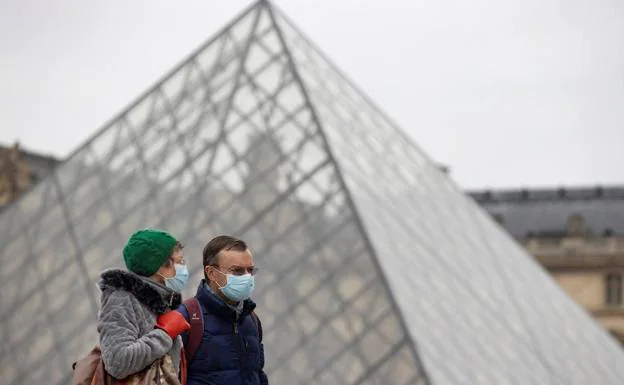 Two tourists walk with masks in front of the Louvre Museum in Paris.