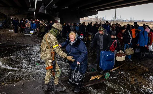 A Ukrainian soldier helps Irpin refugees cross a river.