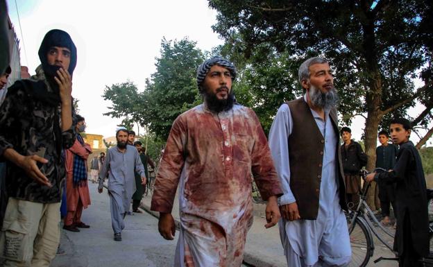 Several people, one of them with his bloody clothes, walk away from the site of the explosion in Kabul.