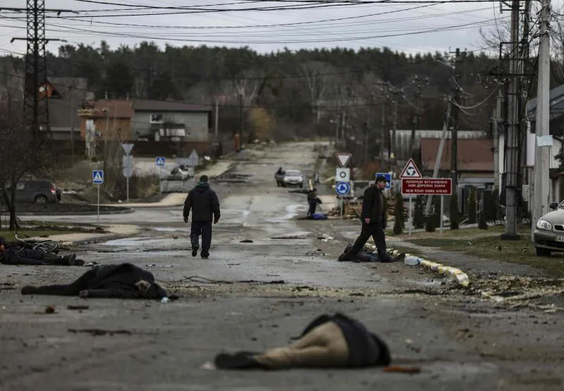 Several citizens walk down a street in Bucha among the bodies of their murdered neighbors