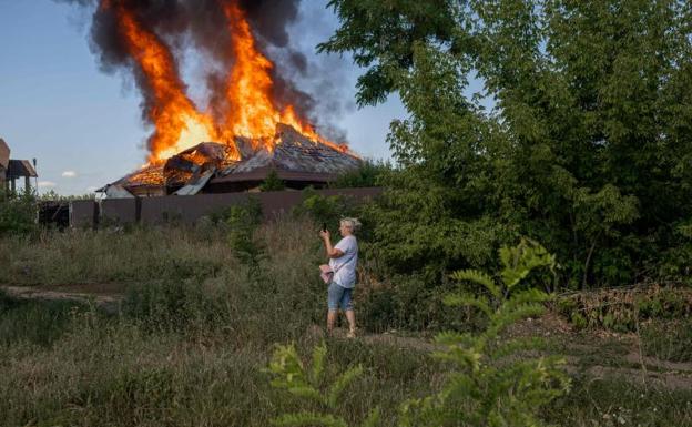 A woman takes a picture of a house that is burning after an attack. 