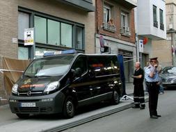 Un Mosso d'Esquadra junto a un furgón de los servicios funerarios en el lugar donde han aparecido los cuerpos de tres personas, presuntamente asesinadas por un ciudadano chino, en el barrio del Carmel. / Efe/